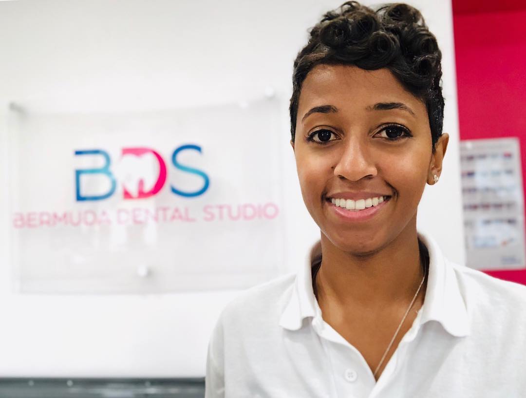 Smiling dental professional standing in front of the Bermuda Dental Studio sign.