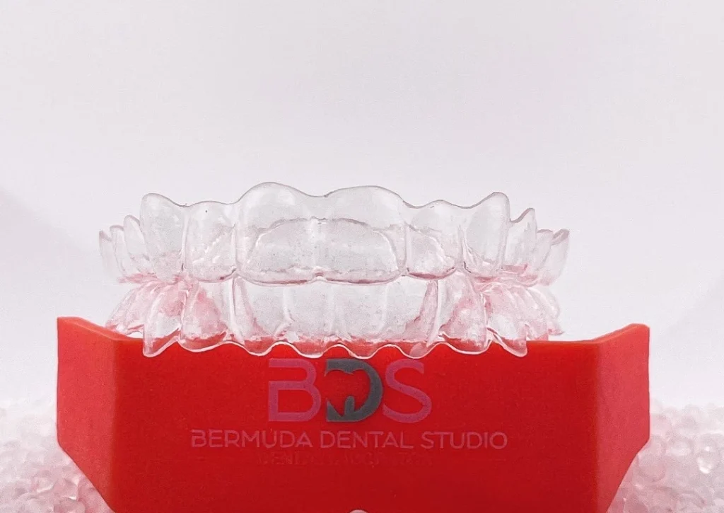 Clear dental aligners displayed on a red stand labeled "Bermuda Dental Studio."